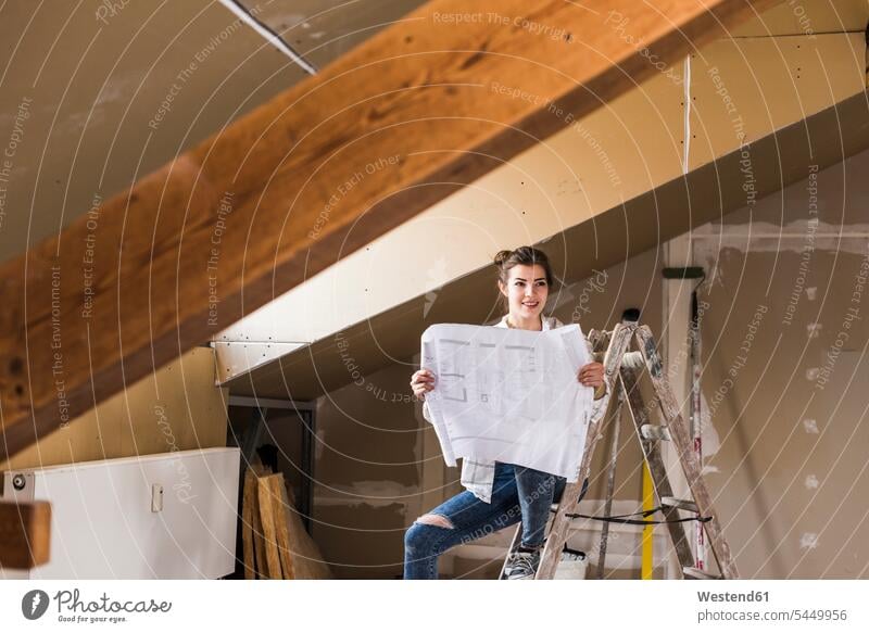 Young woman renovating her new home, holding construction plan young women young woman home ownership private owned home ladder ladders floor plan floor plans