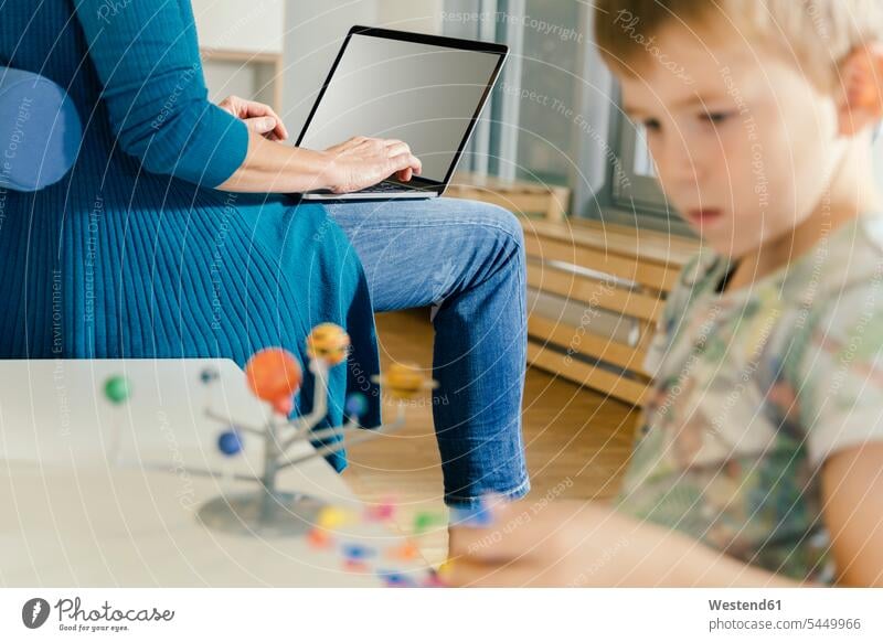 Boy exploring solar system model with woman with laptop in kindergarten models nursery school child children kid kids educator learning pedagogics people