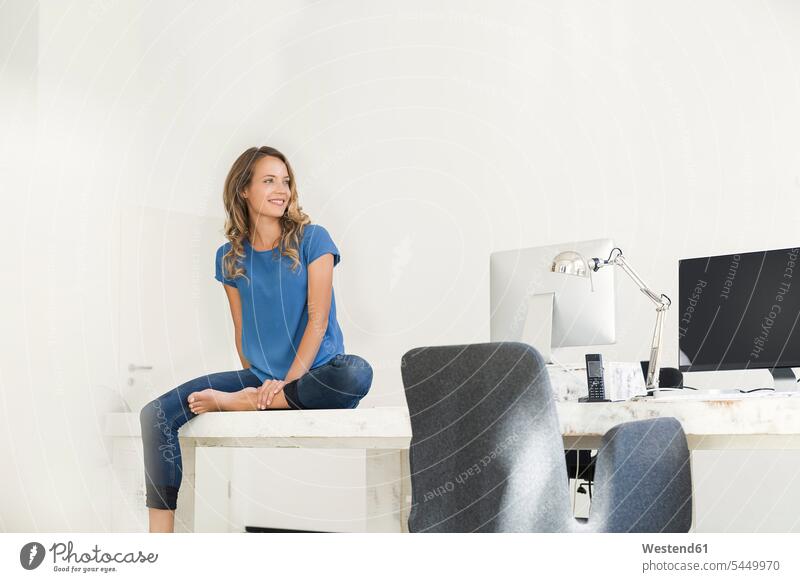 Casual businesswoman in office, sitting on desk, looking confident offices office room office rooms Seated businesswomen business woman business women