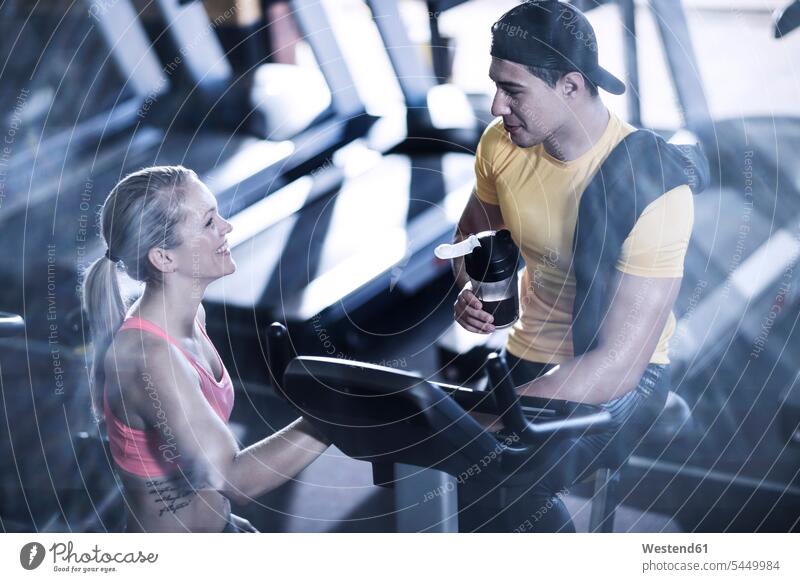 Young man and woman talking in gym gyms Health Club exercise machine exercise machines stationary bike Stationary Bikes smiling smile exercising training