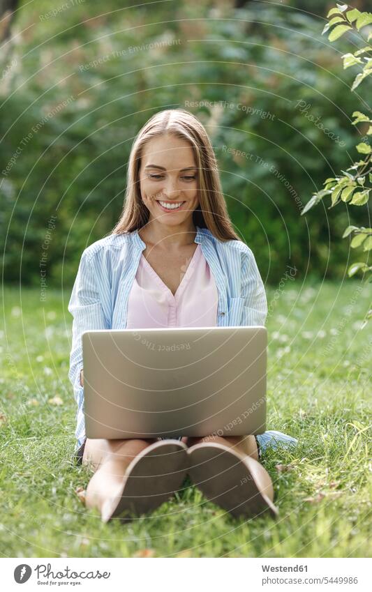 Smiling young woman using laptop on a meadow smiling smile park parks females women Laptop Computers laptops notebook Adults grown-ups grownups adult people