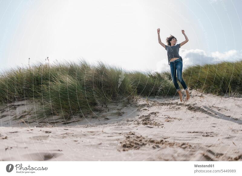 Happy woman jumping in beach dune beaches laughing Laughter females women Leaping sand dune sand dunes positive Emotion Feeling Feelings Sentiments Emotions