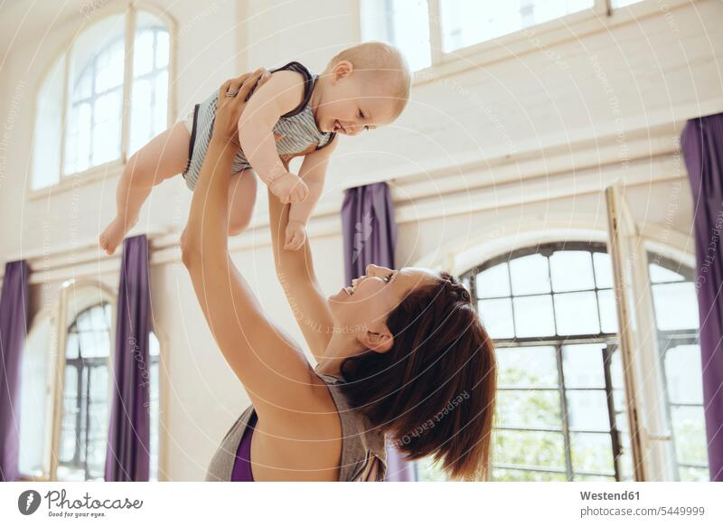 Sporty woman lifting up happy baby in training room exercising exercise practising laughing Laughter infants nurselings babies mother mommy mothers mummy mama