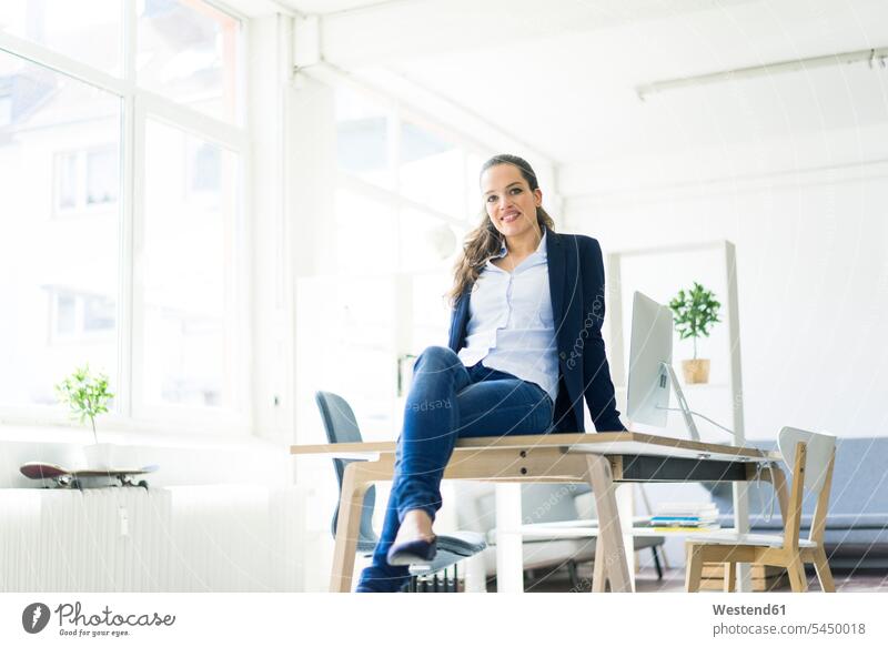 Portrait of smiling businesswoman sitting on table in a loft smile Seated businesswomen business woman business women females business people businesspeople