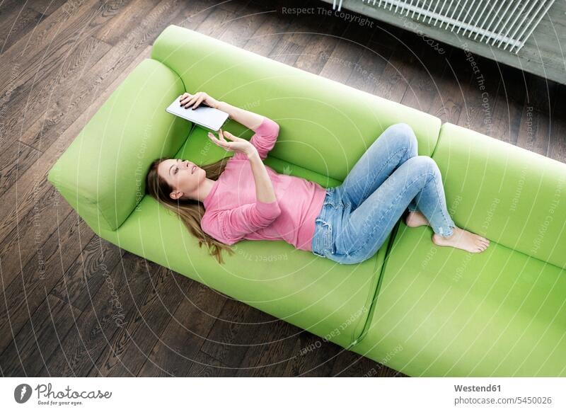 Young woman lying on the couch using tablet settee sofa sofas couches settees females women digitizer Tablet Computer Tablet PC Tablet Computers iPad
