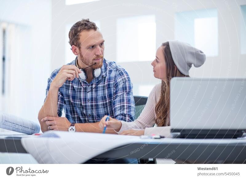 Young man and woman discussing project in design office Office Offices laptop Laptop Computers laptops notebook together working At Work discussion designer