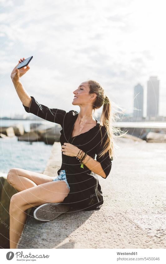 Young woman taking a selfie at the seafront Selfie Selfies females women smiling smile mobile phone mobiles mobile phones Cellphone cell phone cell phones