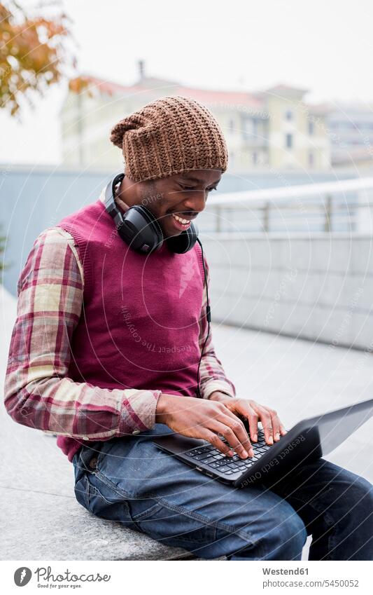 Smiling man with headphones sitting on bench using laptop men males Laptop Computers laptops notebook Adults grown-ups grownups adult people persons human being