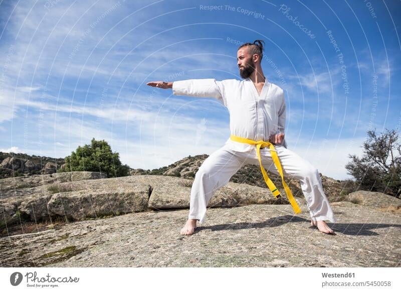 Man doing martial arts poses on a rock exercising exercise training practising standing man men males combative sport fighting Adults grown-ups grownups adult