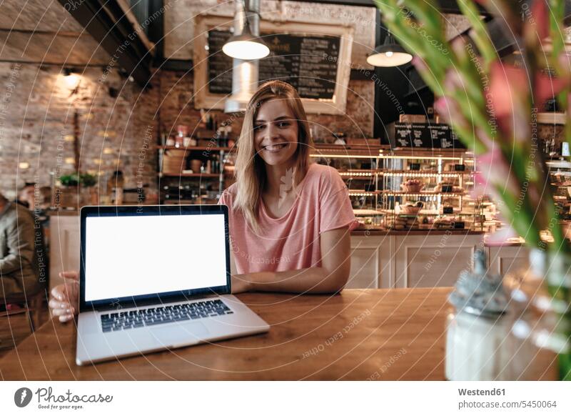 Young woman sitting in cafe, with laptop on table Laptop Computers laptops notebook smiling smile Seated happiness happy females women young computer computers