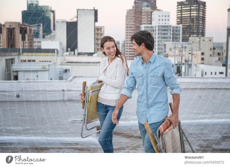 Young couple carrying folding chairs on a rooftop terrace meeting encounter gathering twosomes partnership couples together flirting Flirtation carefree friends