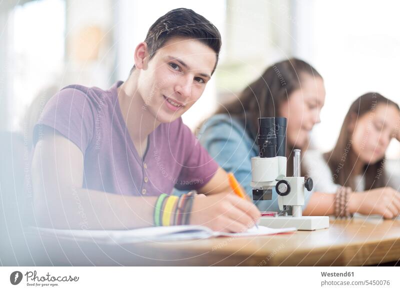 Portrait of smiling science student in class writing write learning microscope microscopes smile pupils education school schools writing down noting front view
