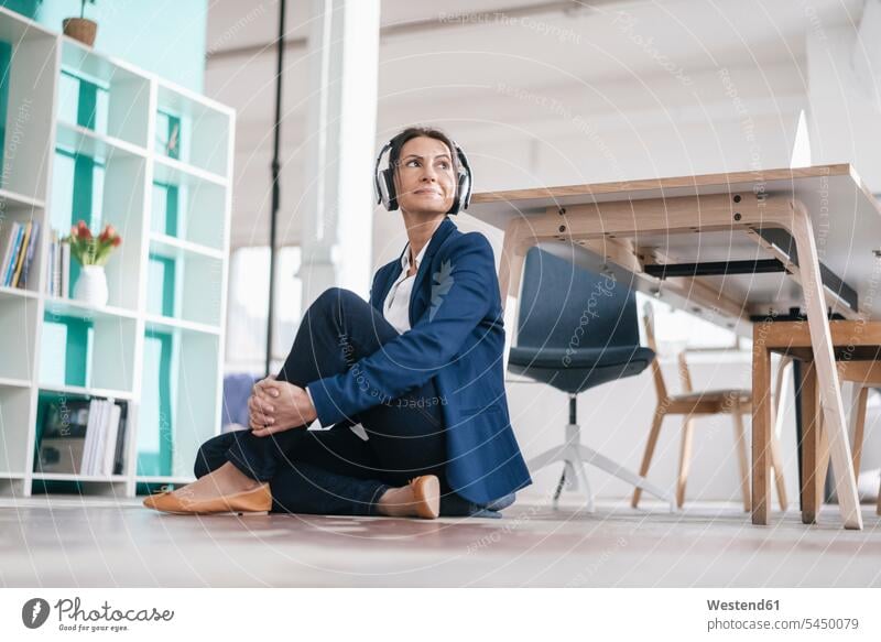 Businesswoman sitting on the floor in a loft listening music with headphones headset businesswoman businesswomen business woman business women females portrait