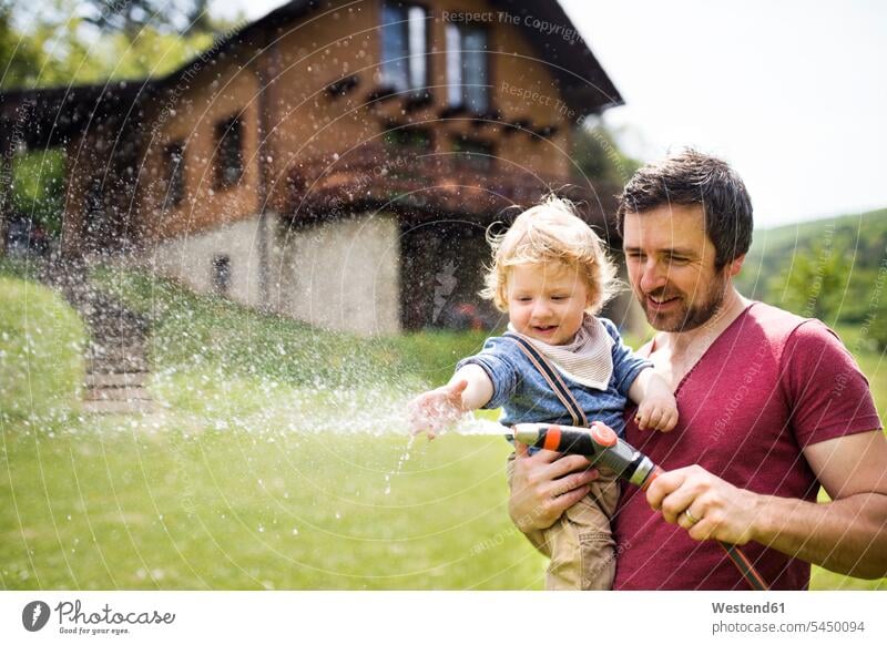 Little boy with his father watering the lawn son sons manchild manchildren hose hoses garden gardens domestic garden pa fathers daddy dads papa family families