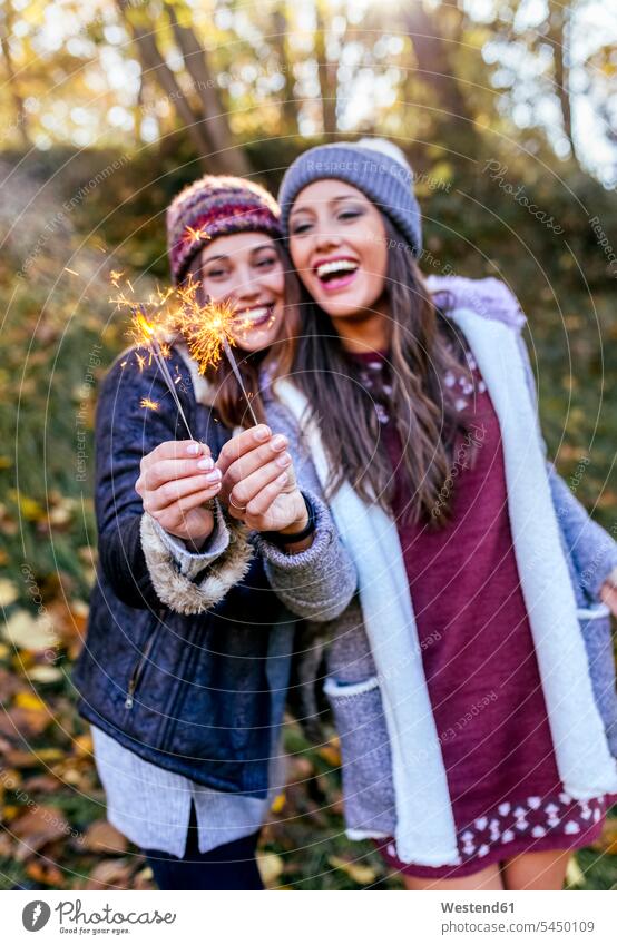 Two happy women holding sparklers in an autumnal forest female friends happiness woods forests woman females beautiful fall mate friendship Adults grown-ups