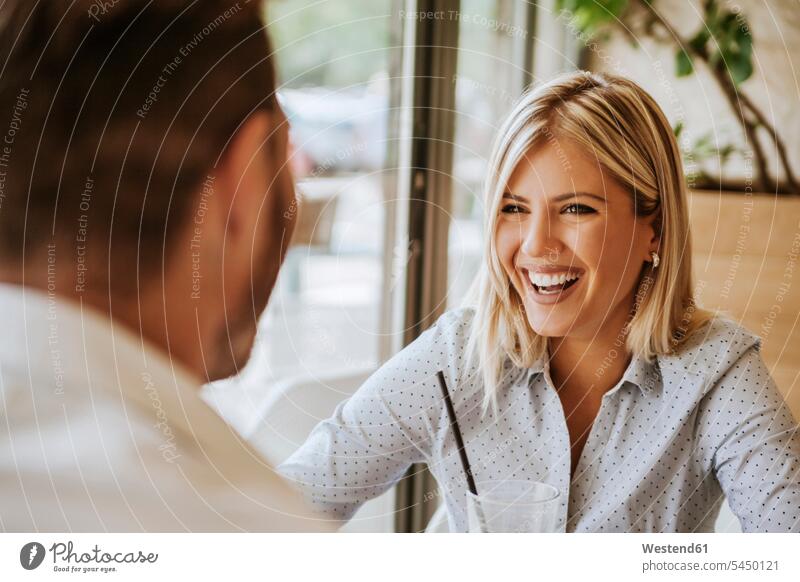 Happy young woman looking at man in a cafe couple twosomes partnership couples talking speaking laughing Laughter people persons human being humans human beings