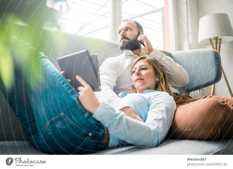 Couple using tablet and cell phone on couch settee sofa sofas couches settees digitizer Tablet Computer Tablet PC Tablet Computers iPad Digital Tablet