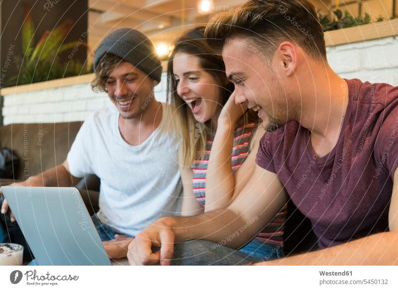Three excited friends looking at laptop in a cafe Laptop Computers laptops notebook happiness happy excitement Exciting friendship computer computers