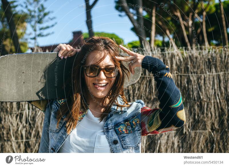 Portrait of young woman with skateboard on her shoulders showing victory sign Skate Board skateboards V sign v-sign portrait portraits on shoulders females