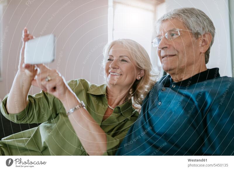 Senior couple at home sitting on couch taking a selfie mobile phone mobiles mobile phones Cellphone cell phone cell phones Selfie Selfies twosomes partnership
