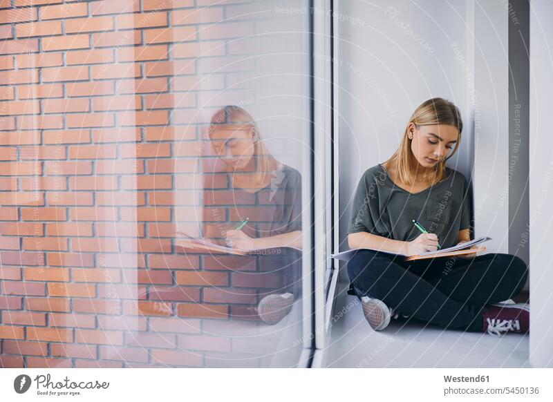 Student sitting at the window in hallway learning documents Seated studying student students female students windows corridor corridors hallways