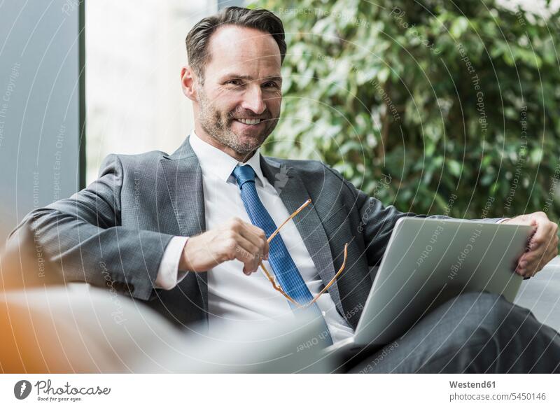 Portrait of smiling businessman sitting in lobby with laptop smile portrait portraits Businessman Business man Businessmen Business men business people