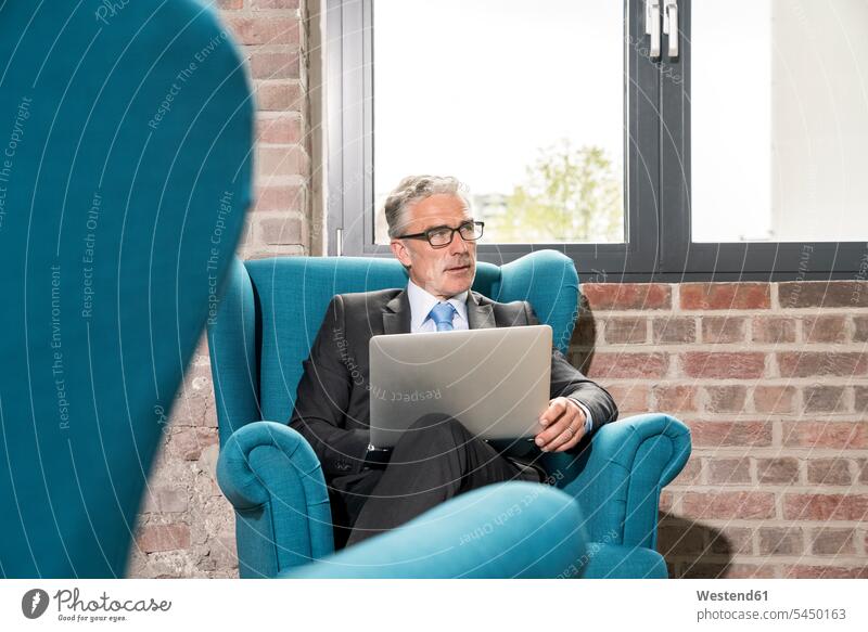 Mature businessman sitting in arm chair, using laptop Laptop Computers laptops notebook Seated armchair Arm Chairs armchairs glasses specs Eye Glasses