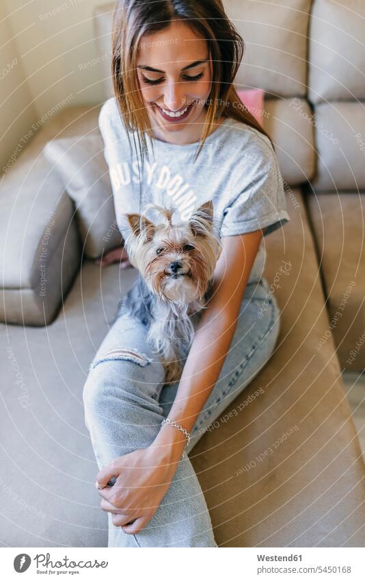 Smiling young woman sitting on couch with her Yorkshire Terrier dog dogs Canine settee sofa sofas couches settees females women pets animal creatures animals