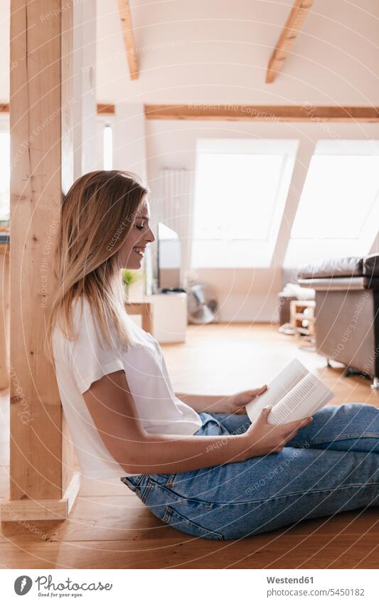 Young woman sitting on floor, reading book cozy sociable comfortable cosy smiling smile books Seated females women home at home Adults grown-ups grownups adult