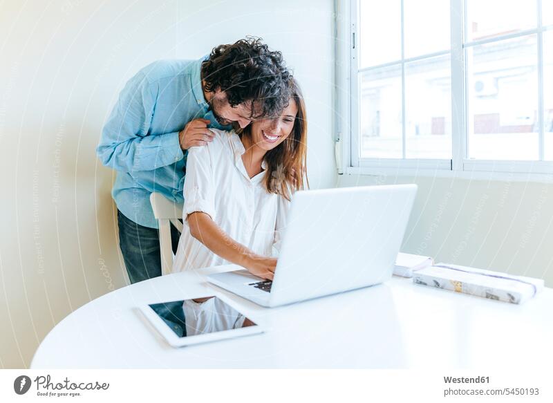 Man embracing woman while working with laptop couple twosomes partnership couples Laptop Computers laptops notebook people persons human being humans