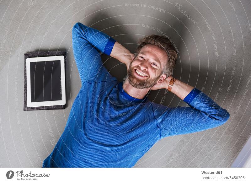 Smiling man lying on the floor next to tablet relaxed relaxation floors break men males laying down lie lying down digitizer Tablet Computer Tablet PC