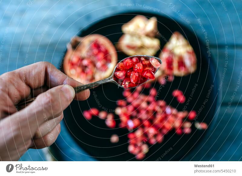 Man's hand holding a tea spoon of pomegranate seed human hand hands human hands men males people persons human being humans human beings Adults grown-ups