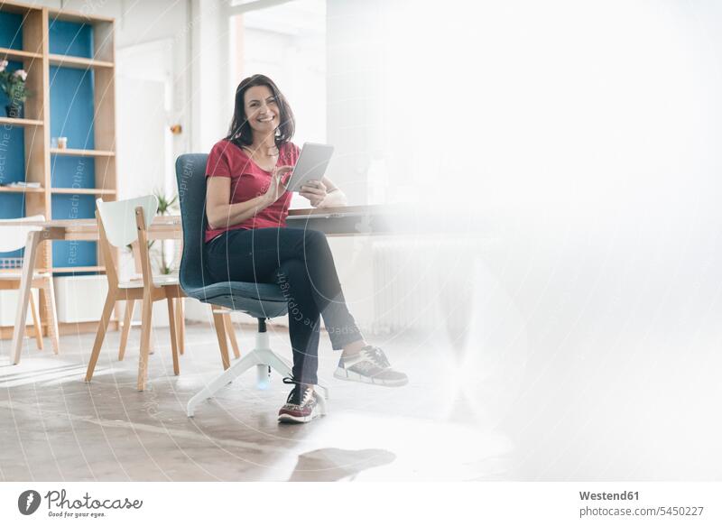 Portrait of smiling woman with tablet sitting at desk in a loft lofts females women Adults grown-ups grownups adult people persons human being humans