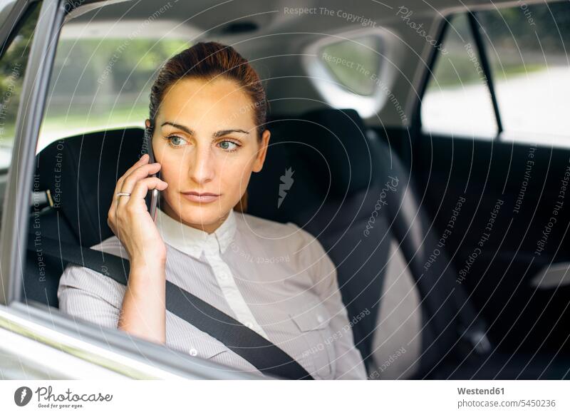 Businesswoman on the phone sitting on backseat of a car businesswoman businesswomen business woman business women automobile Auto cars motorcars Automobiles