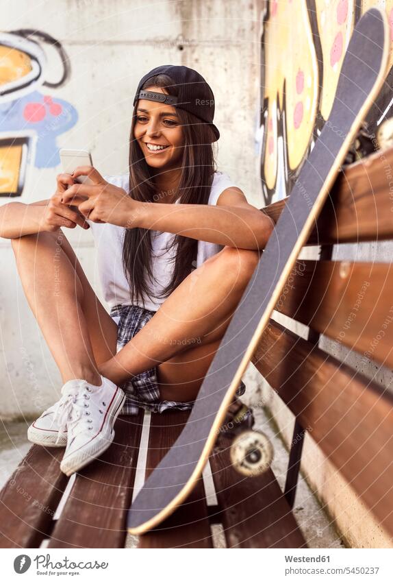 Smiling young woman with skateboard looking at cell phone smiling smile Skate Board skateboards mobile phone mobiles mobile phones Cellphone cell phones bench