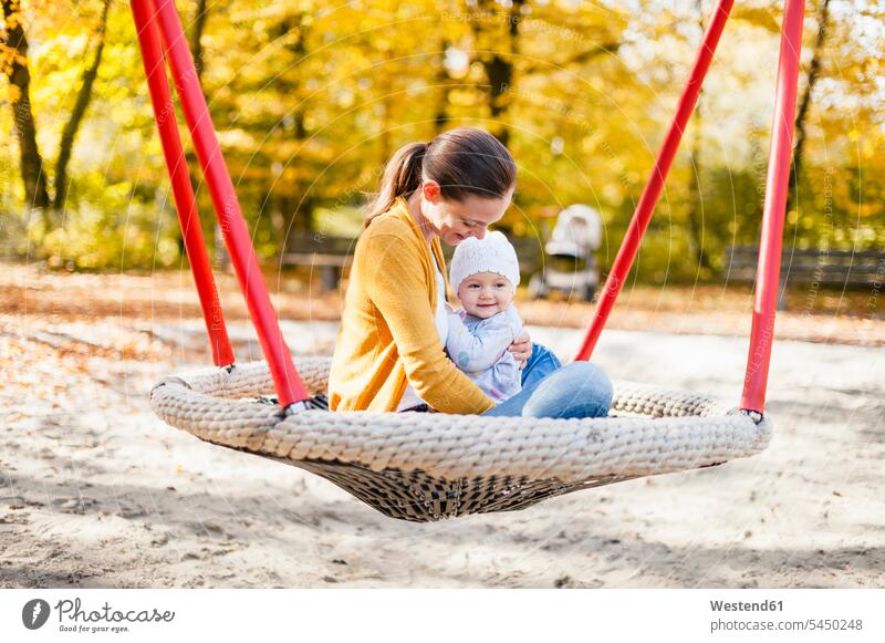 Happy baby girl relaxing with her mother on a swing in autumn happiness happy playground play yard play ground playgrounds mommy mothers ma mummy mama infants