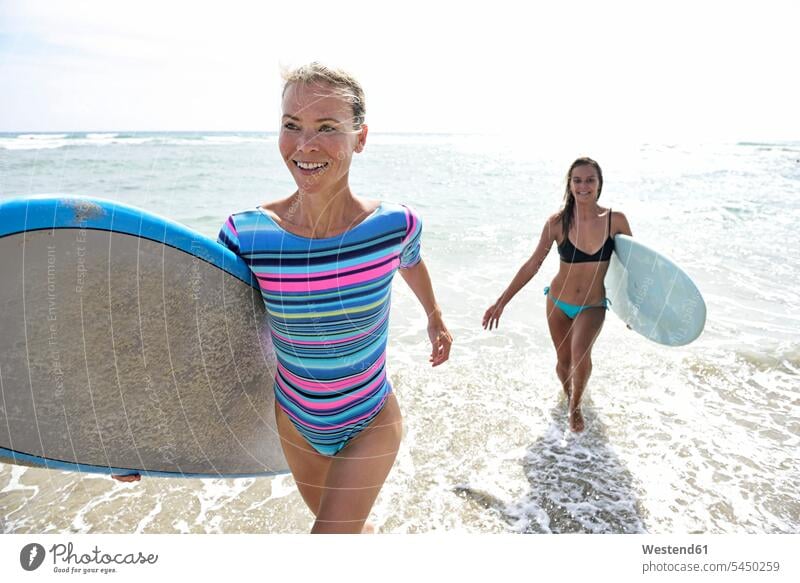 Two women in the sea with surfboards smiling smile female friends woman females surfing surf ride surf riding Surfboarding running water sports Water Sport