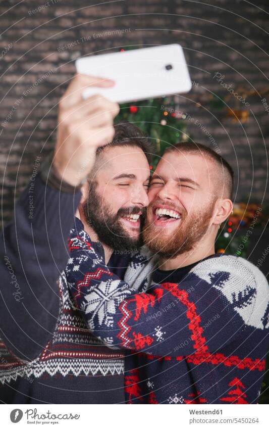 Portrait of laughing gay couple taking selfie with smartphone at Christmas time at home Gay Couple Gays Selfie Selfies Laughter same-sex couple woman and woman
