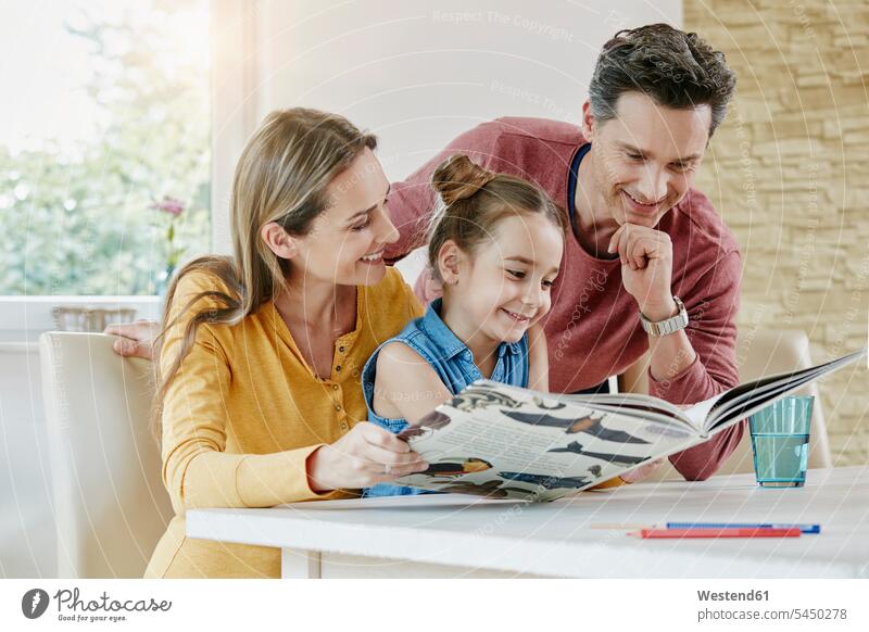 Happy family at home looking at picture book books eyeing happiness happy reading daughter daughters families smiling smile view seeing viewing child children