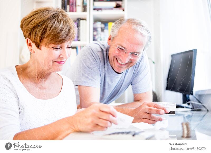 Senior couple at desk paying bills twosomes partnership couples smiling smile people persons human being humans human beings invoices finances financial casual