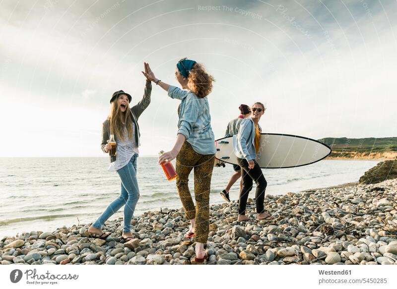 Excited friends with surfboard and drinks on stony beach beaches happiness happy surfer surfers surfboards friendship surfing surf ride surf riding Surfboarding