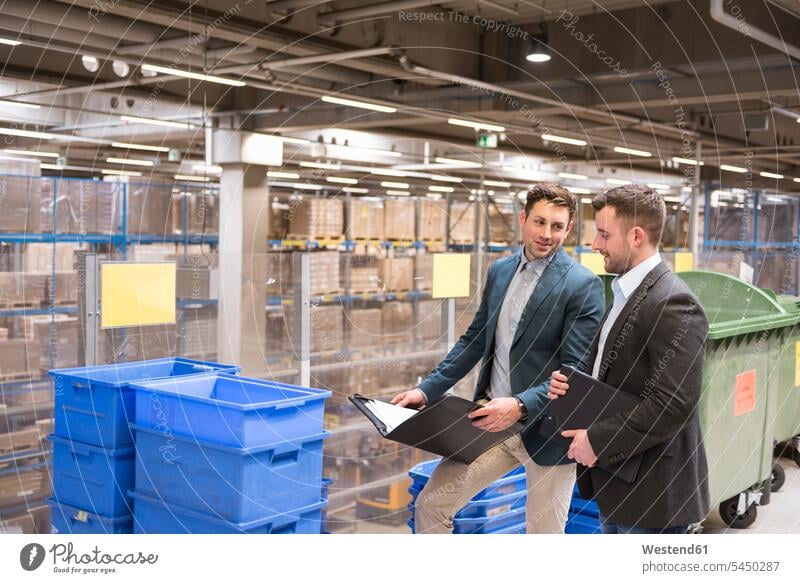 Two businessmen with documents talking in factory warehouse speaking man males working At Work colleagues smiling smile storehouse storage Adults grown-ups