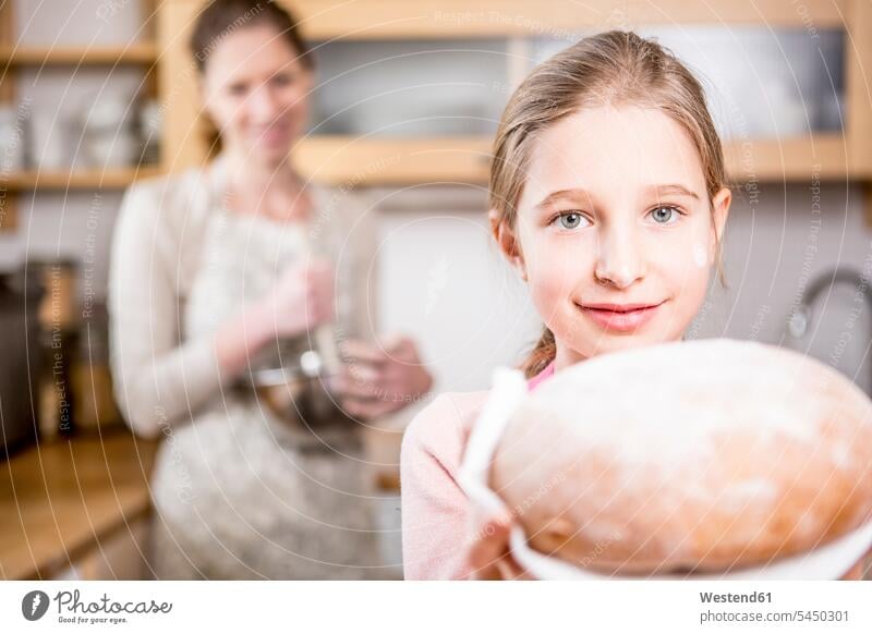 Girl holding bread in kitchen with mother in background daughter daughters Bread Breads girl females girls domestic kitchen kitchens child children family