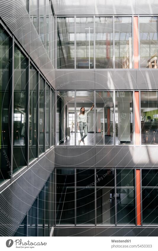 Woman standing at office window, looking up businesswoman businesswomen business woman business women glass pane glass panes offices office room office rooms