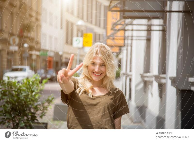 Portrait of happy blond woman showing victory sign V sign v-sign portrait portraits females women Hand Sign hand gesture hand signal Adults grown-ups grownups