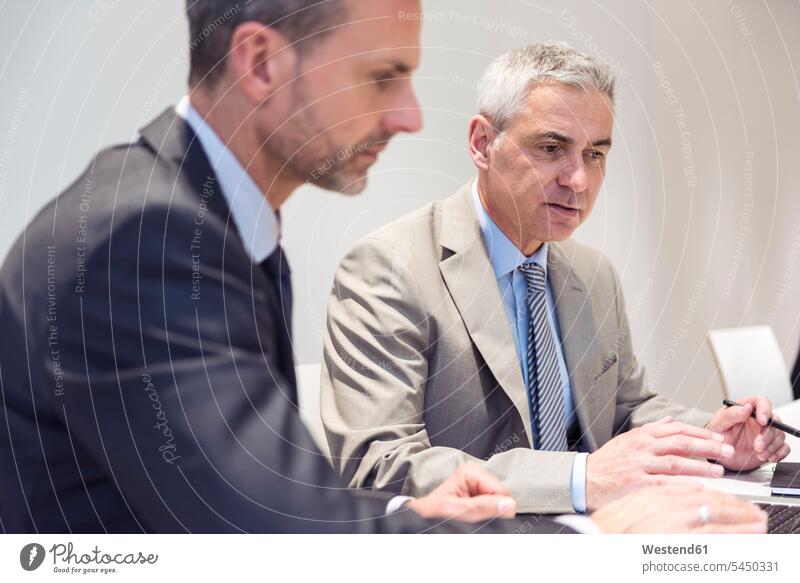 Two businessmen working together in office sitting Seated At Work offices office room office rooms discussing discussion expertise competence competent