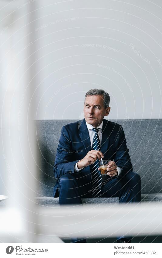 Mature businessman with glass of coffee sitting on couch in his office looking out of window portrait portraits Businessman Business man Businessmen