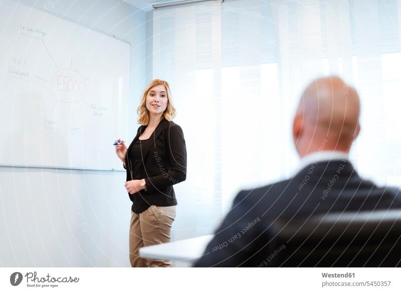 Businessman looking at businesswoman at whiteboard in office businesswomen business woman business women writing write offices office room office rooms talking