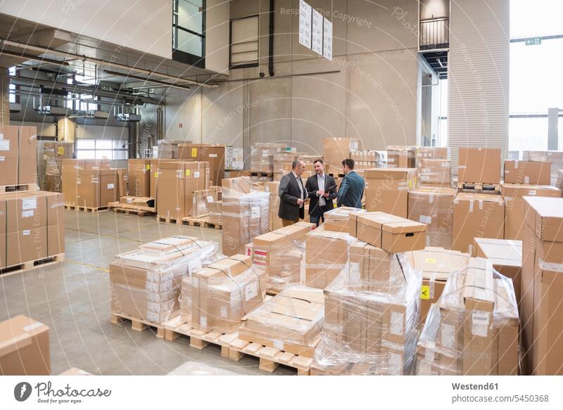 Three men in factory warehouse surrounded by cardboard boxes working At Work man males colleagues Businessman Business man Businessmen Business men talking
