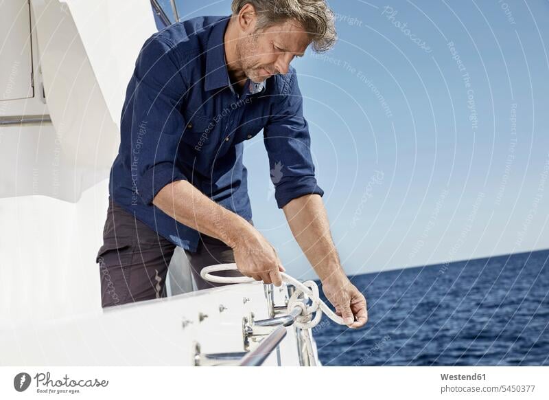 Man on motor yacht tying a knot man men males motor yachts Adults grown-ups grownups adult people persons human being humans human beings Yacht Yachts ship